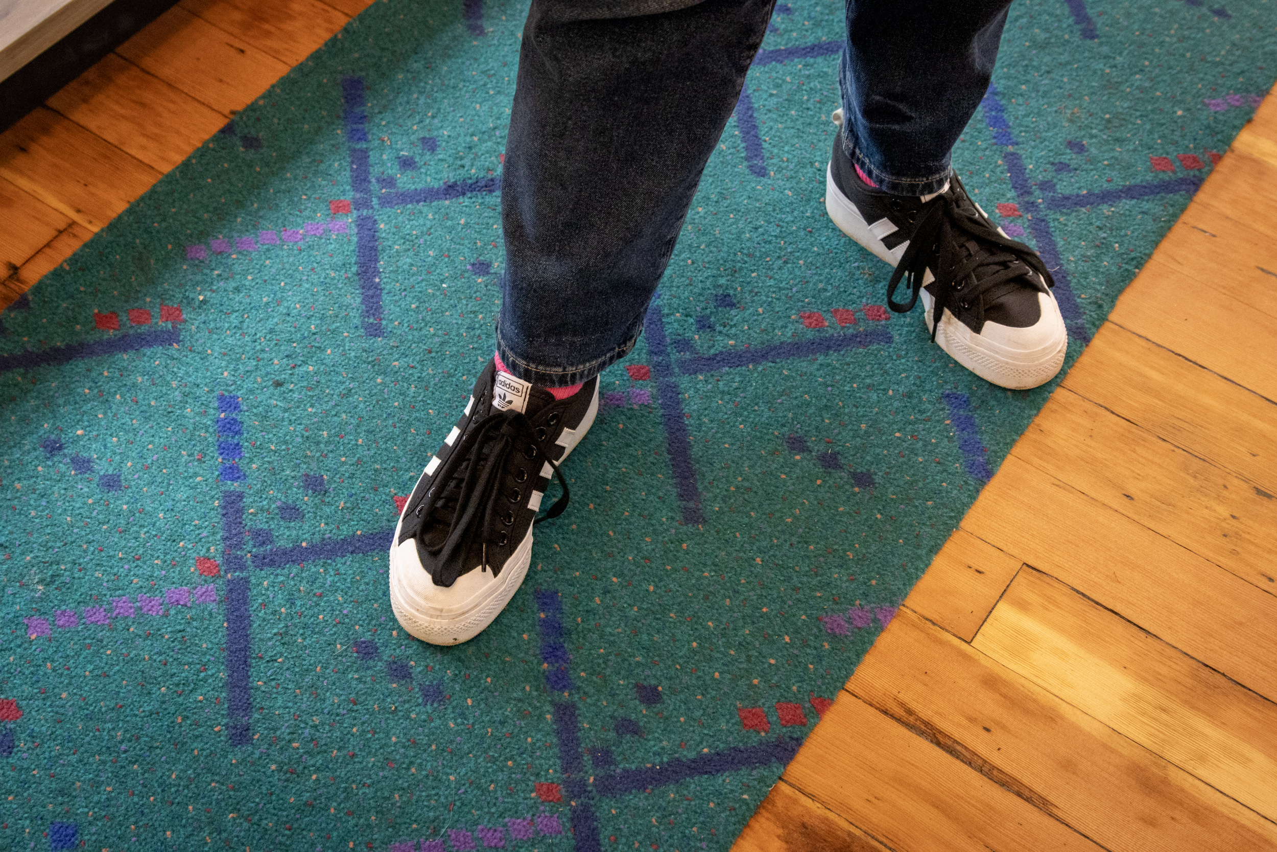 A person wearing black and white sneakers standing on the old PDX (Portland International Airport) carpet.